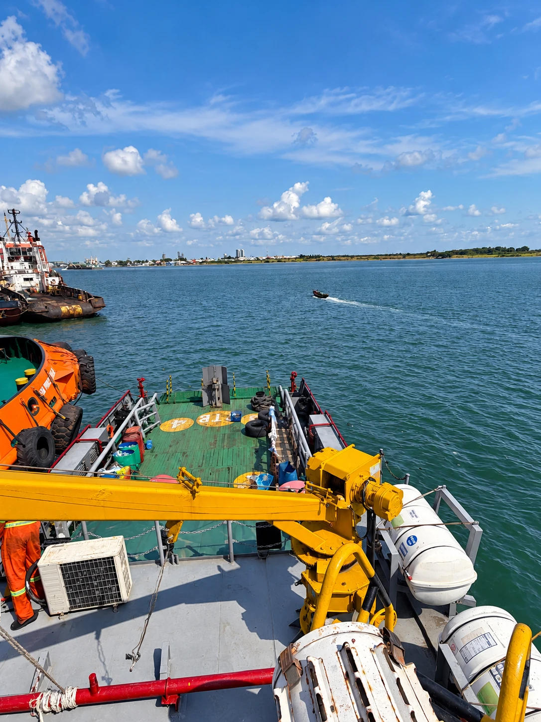 Vessel deck, crane, lifeboat and life rafts overlooking the harbour
